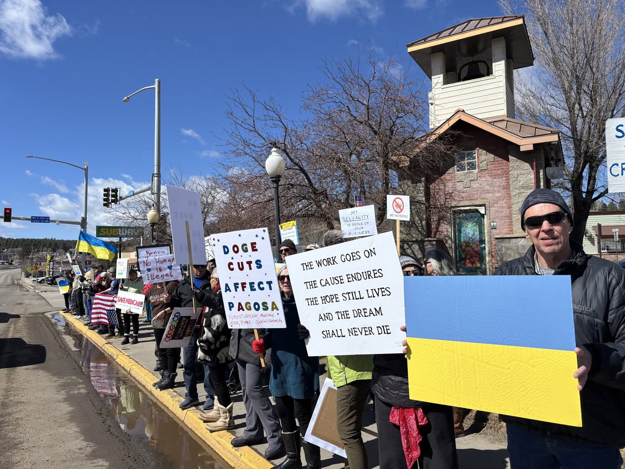 Protesters stand along 160 holding signs protesting the Trump administration 